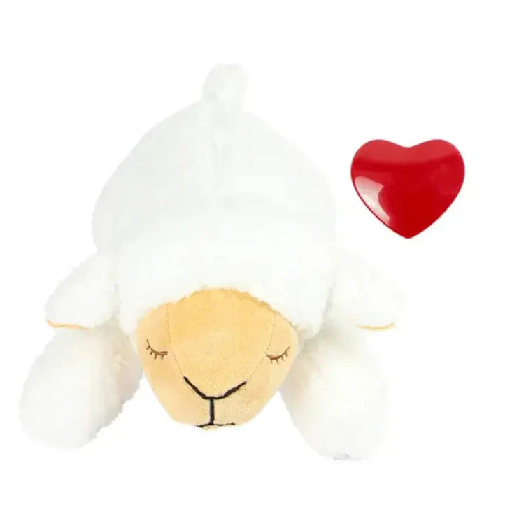 Plush toy lamb with closed eyes lying next to a red heart shape.