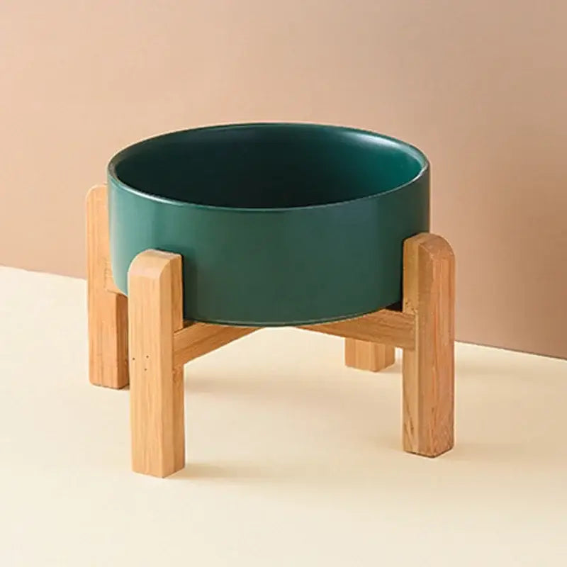 Green ceramic bowl on a wooden stand with four legs.