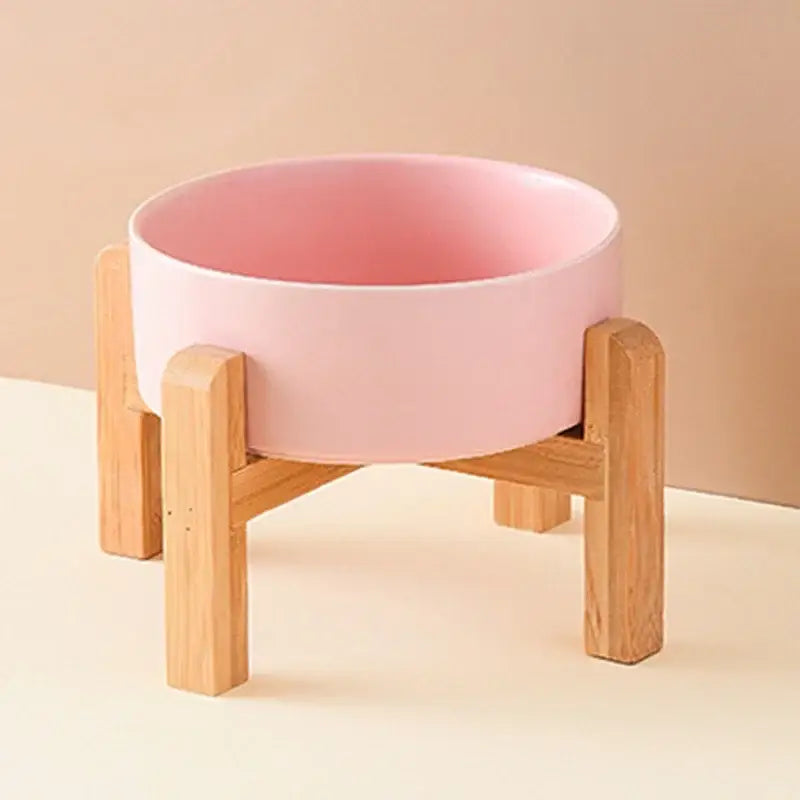 Pink ceramic bowl on a wooden stand with four legs.