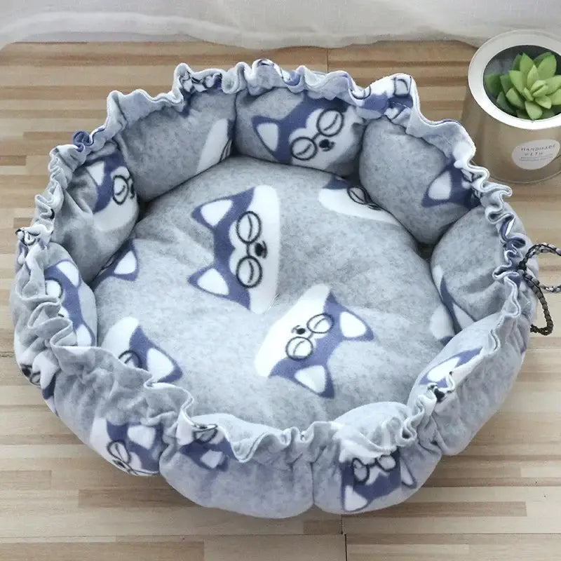 Circular pet bed with cat face designs on gray fabric.