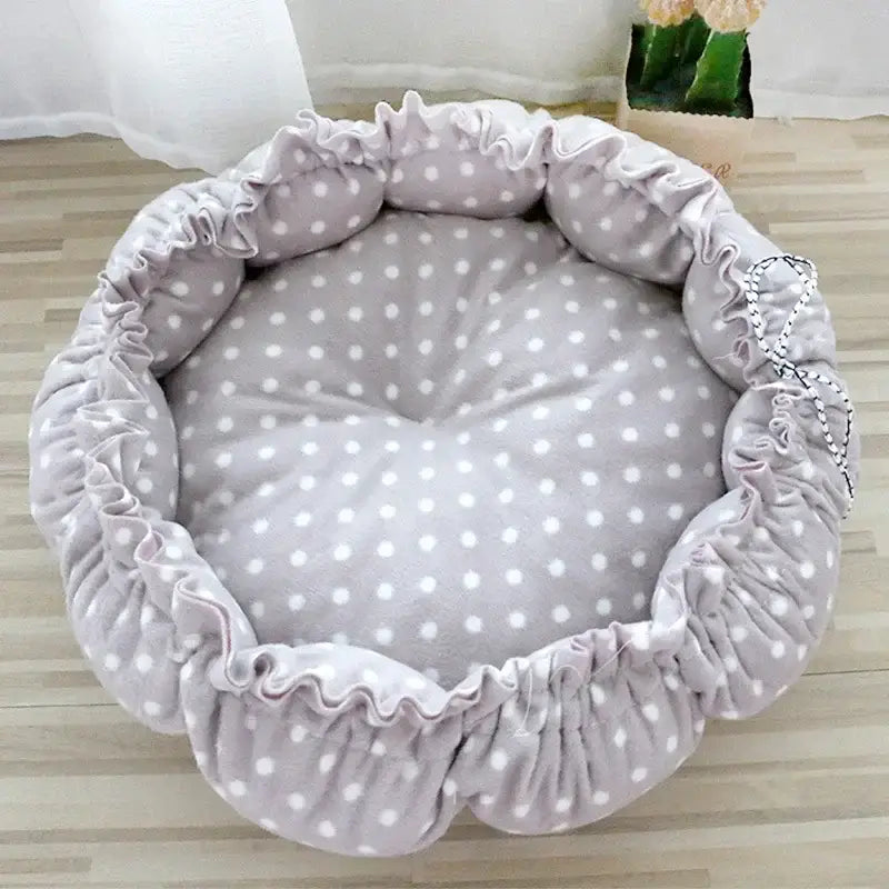 Circular pet bed with gray polka dot fabric and ruffled edges.