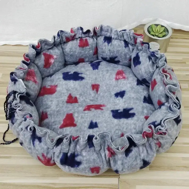 Circular pet bed with a gray, red, and blue patterned fabric and ruffled edges.