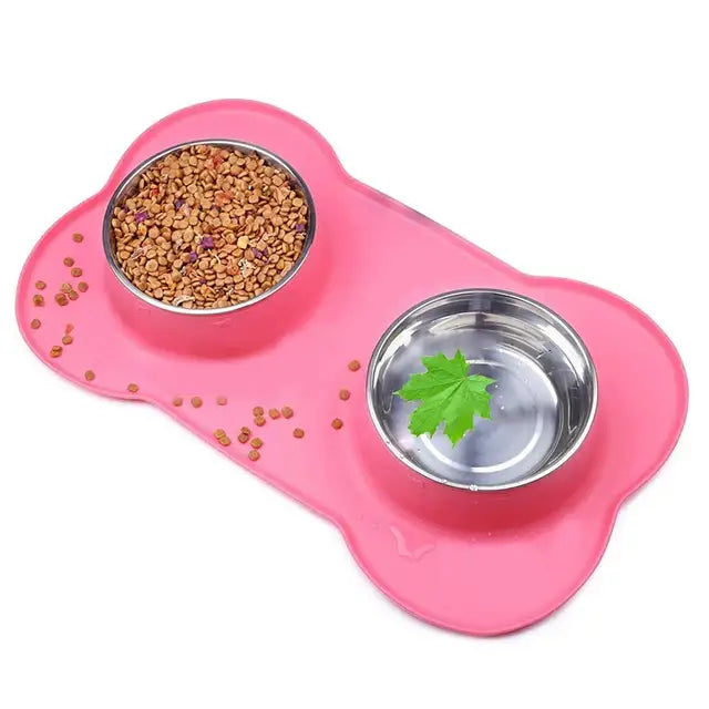 Pink bone-shaped pet feeding mat with two metal bowls, one containing dry food and the other water with a leaf.