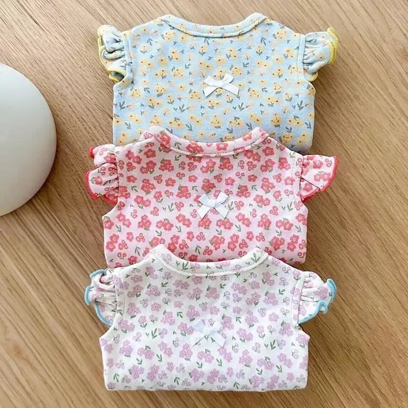 Three floral-patterned baby onesies in pastel colors.