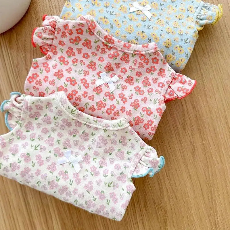 Three floral-patterned baby onesies or bodysuits laid out on a wooden surface.