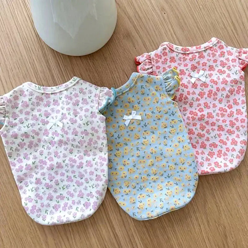 Three infant onesies with floral patterns in pink, blue, and white.