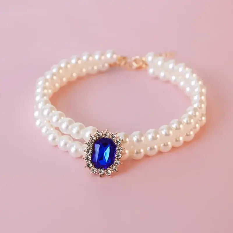 Pearl bracelet with a blue gemstone centerpiece surrounded by small diamonds.