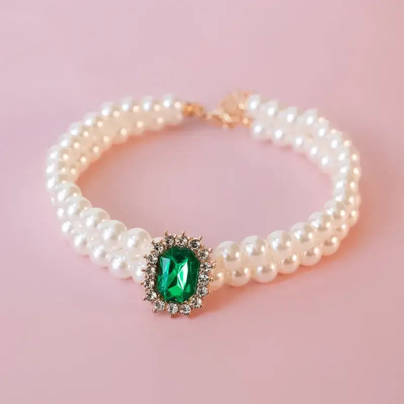 Pearl bracelet featuring a central emerald gemstone surrounded by diamonds.