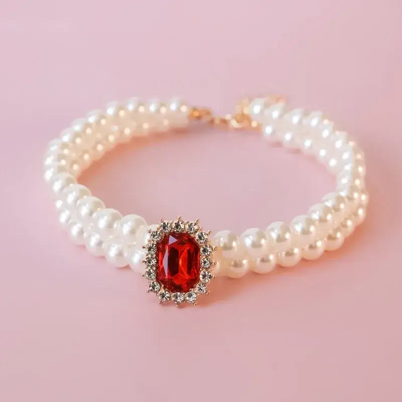 Pearl bracelet with a central red gemstone surrounded by smaller clear stones.