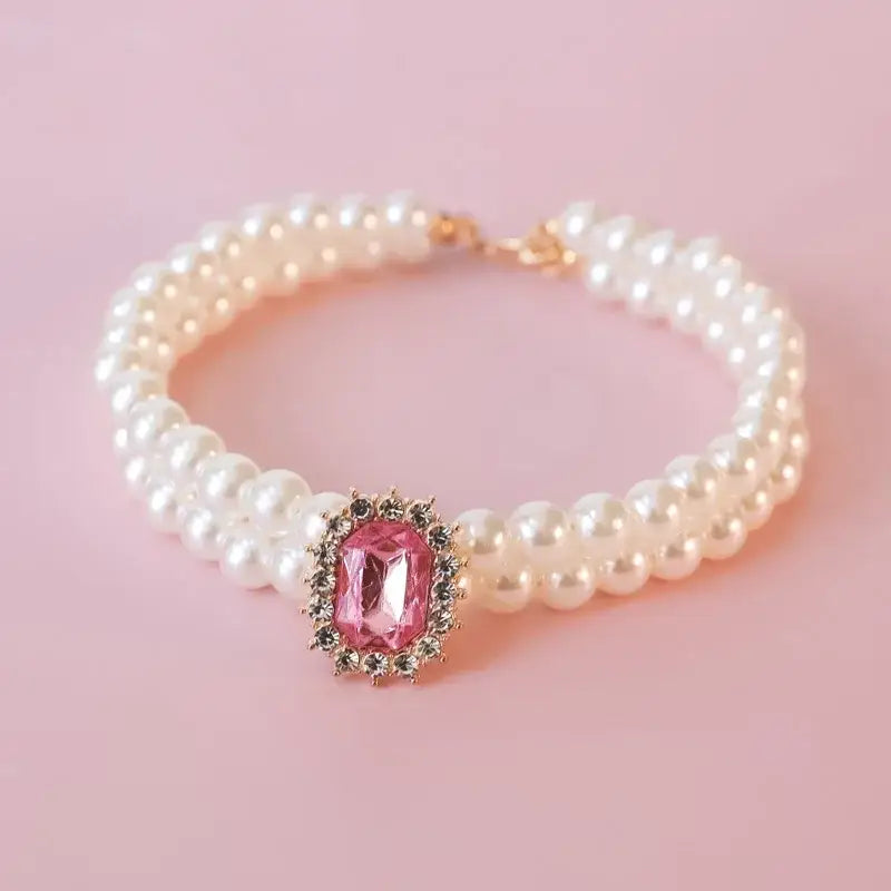 Pearl bracelet with a pink gemstone centerpiece surrounded by smaller crystals.