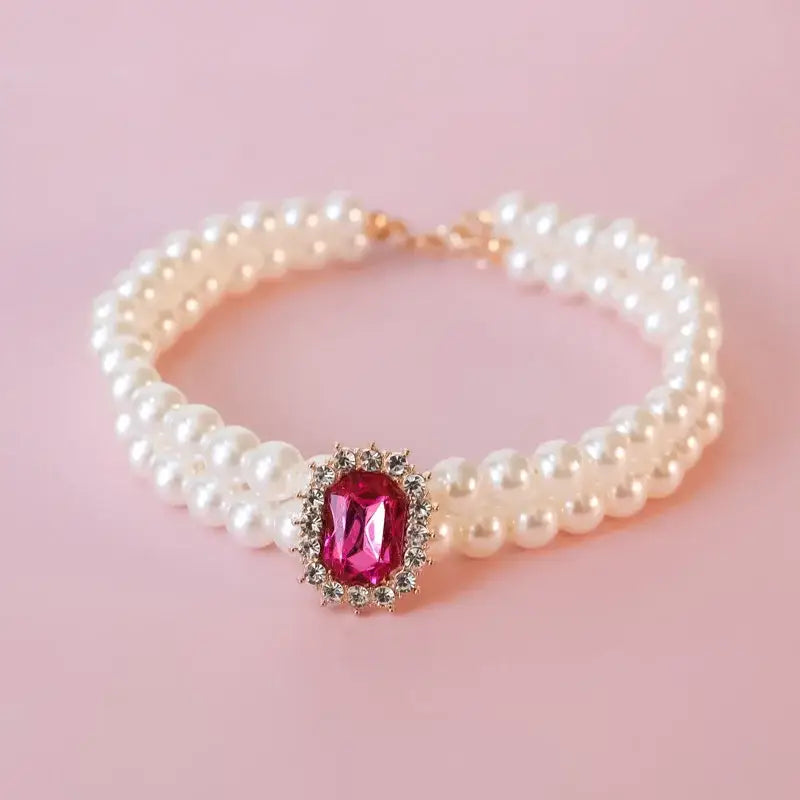 Pearl bracelet with a pink gemstone centerpiece surrounded by smaller crystals.