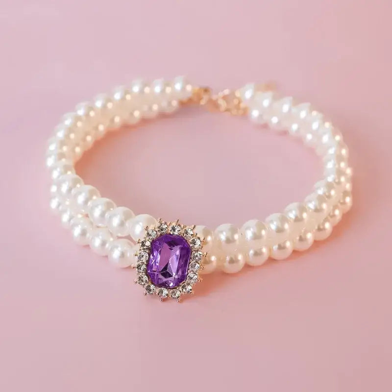 Pearl bracelet with a purple gemstone centerpiece surrounded by small diamonds.