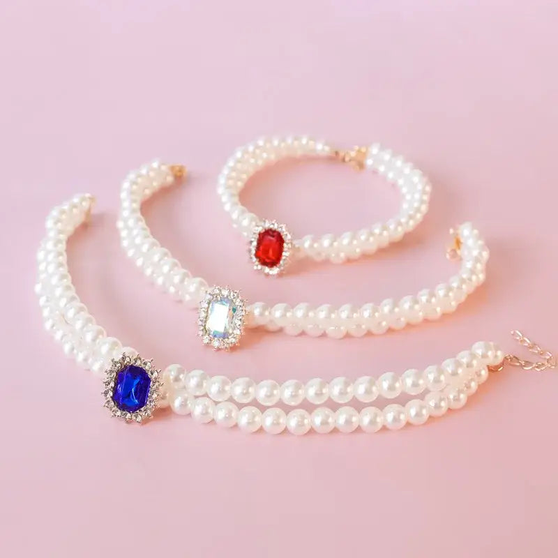 Three pearl bracelets with colorful gemstone centerpieces.