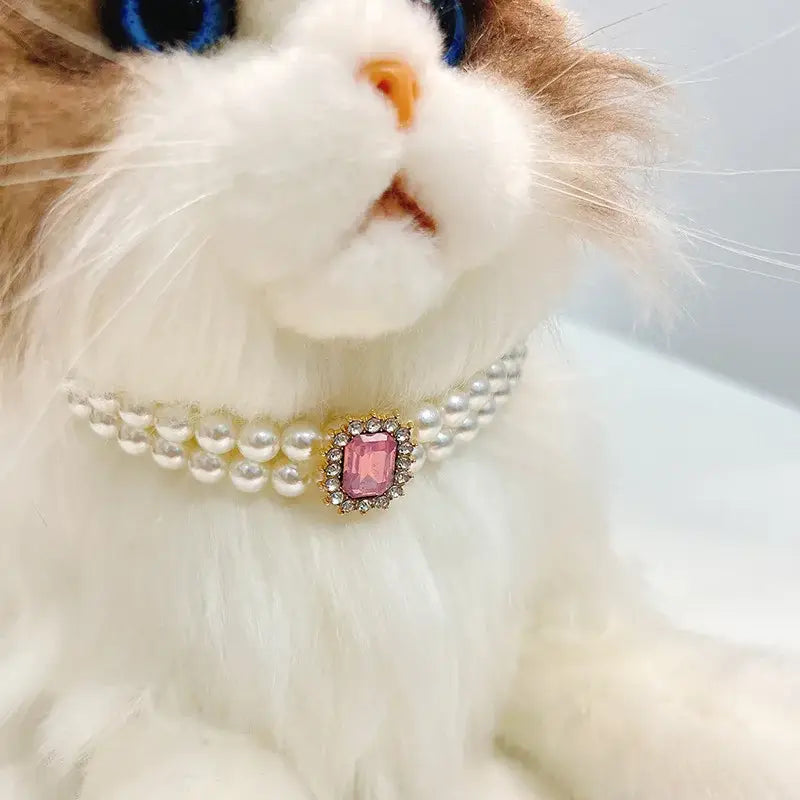 White cat wearing a pearl necklace with a pink gemstone pendant.