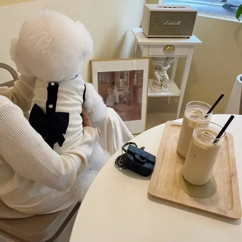 Plush toy with a round white head wearing a white sweater and black bow tie.