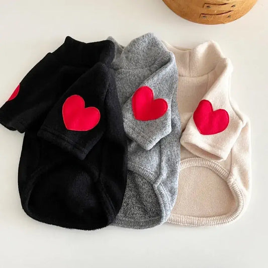 Three dog sweaters with red heart patches in black, gray, and white colors.