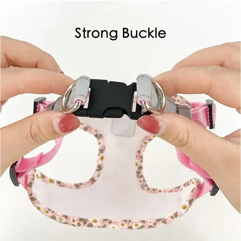 A pink pet collar with a black plastic buckle being fastened by hands with red nail polish.