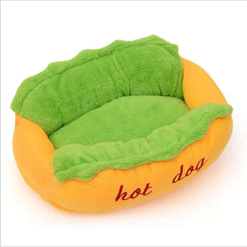 Plush hot dog-shaped pet bed with green cushioning and ’hot dog’ text.