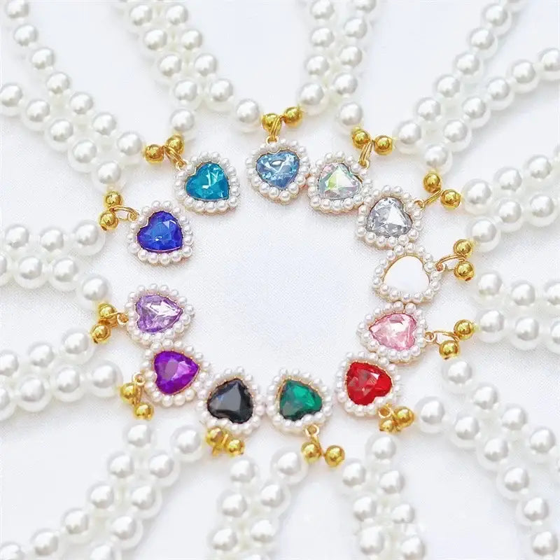 Heart-shaped gemstone pendants on pearl necklaces arranged in a circular pattern.