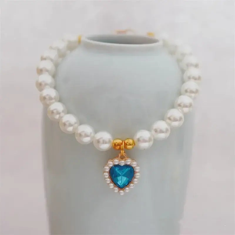 Pearl necklace with a blue heart-shaped pendant surrounded by smaller gems.