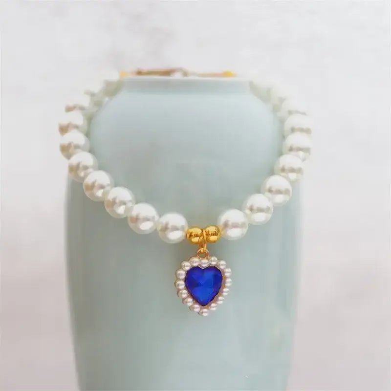 Pearl necklace with a blue heart-shaped pendant surrounded by small diamonds.