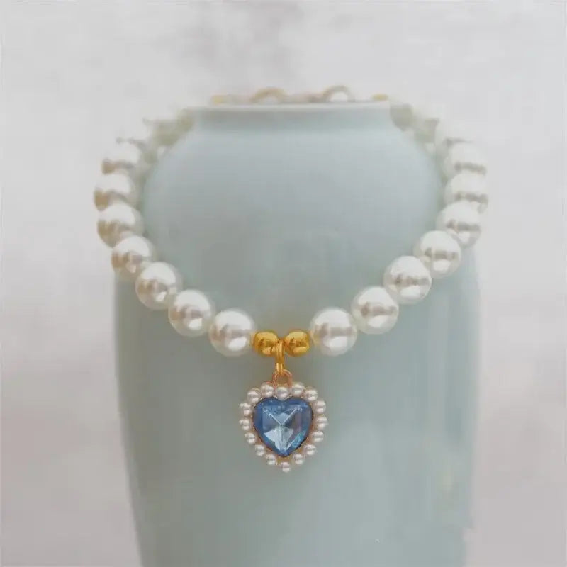 Pearl necklace with a heart-shaped blue gemstone pendant surrounded by smaller pearls.