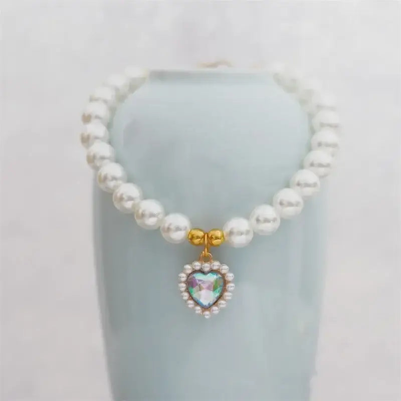 Pearl necklace with a heart-shaped pendant featuring a gemstone center surrounded by smaller stones.