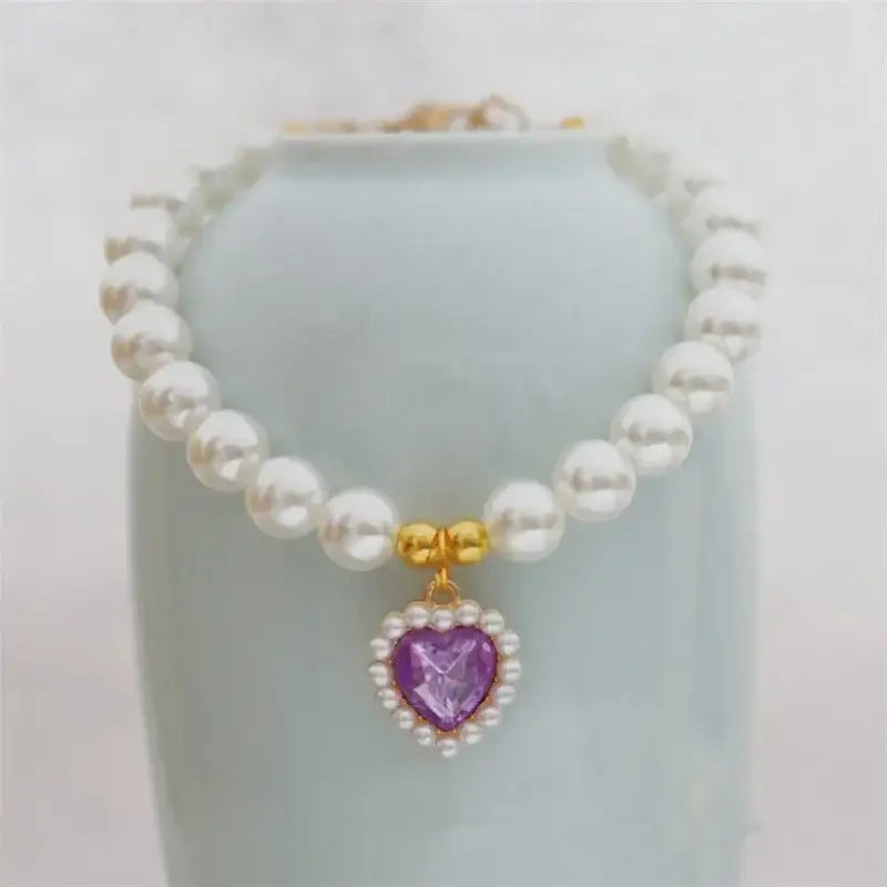 Pearl necklace with a heart-shaped purple gemstone pendant surrounded by smaller white gems.