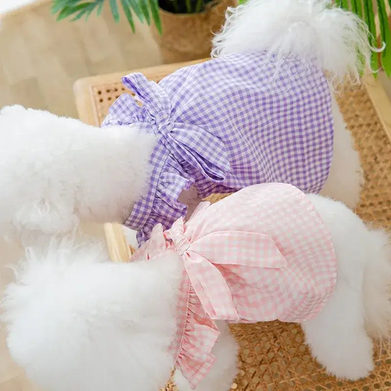 Plush or stuffed white dog toy wearing purple and pink gingham outfits.