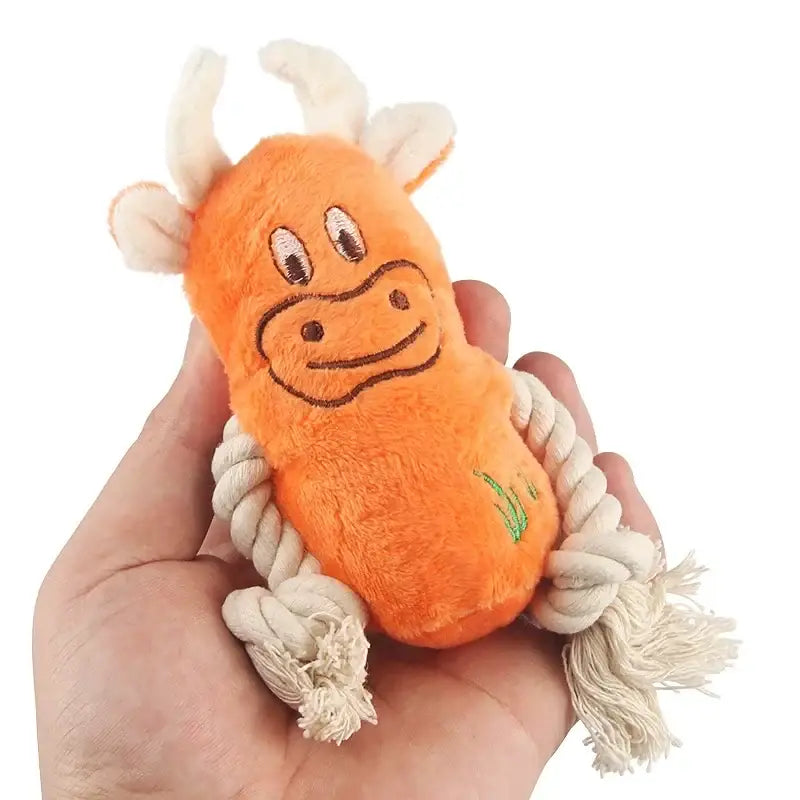 Orange plush cow toy with rope legs held in a hand.