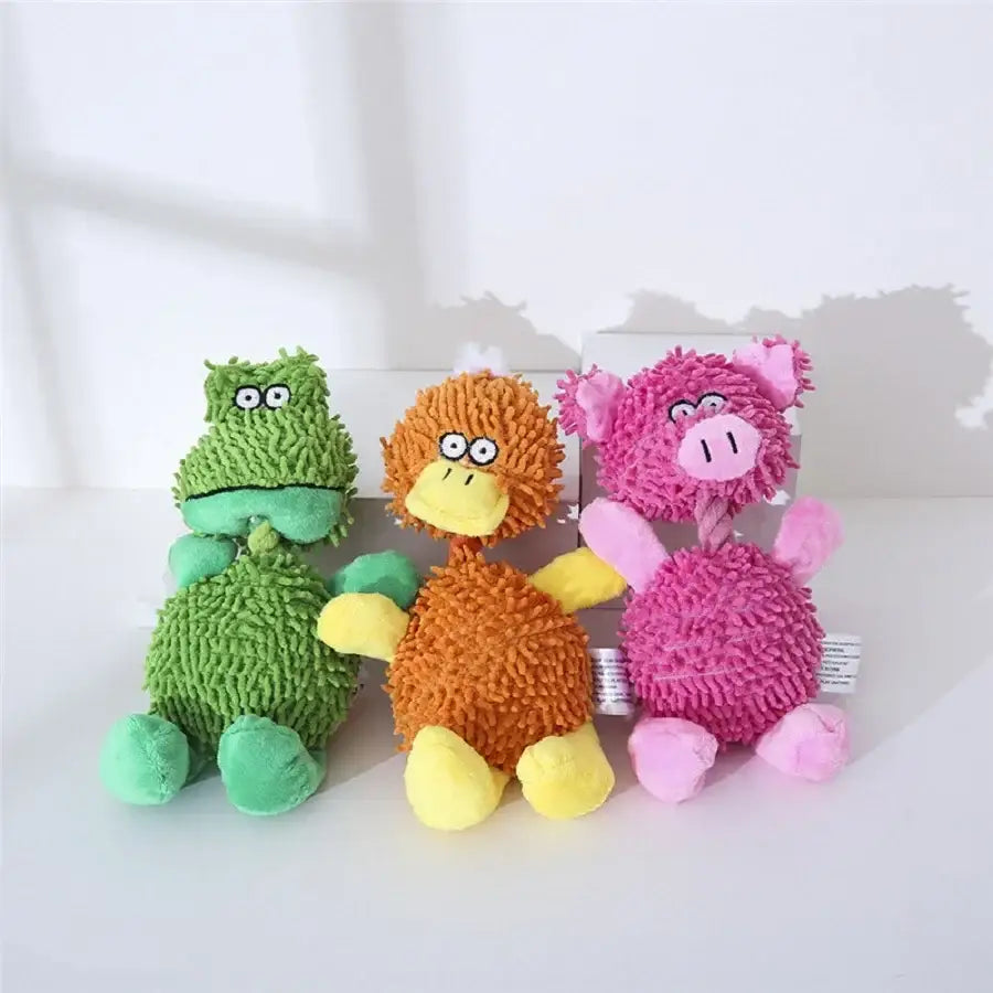 Three colorful plush toy animals sitting together - a green frog, an orange duck, and a pink pig.