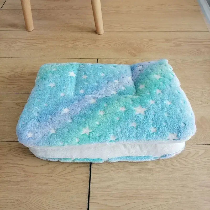 Plush, pastel-colored blanket with a star pattern folded on a wooden floor.