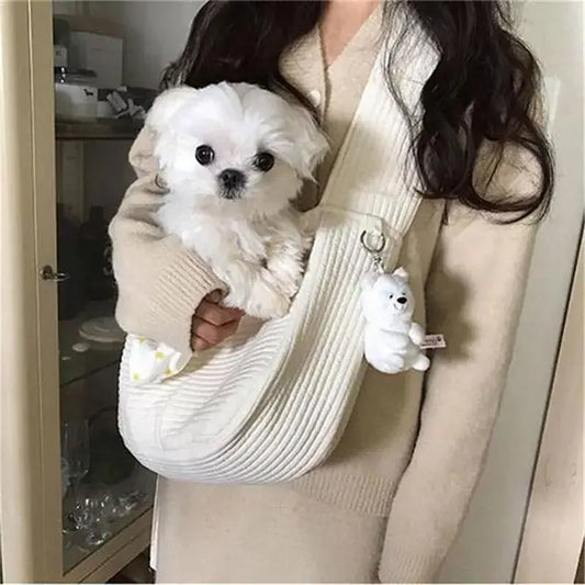 Fluffy white puppy being held in a knitted sling carrier.