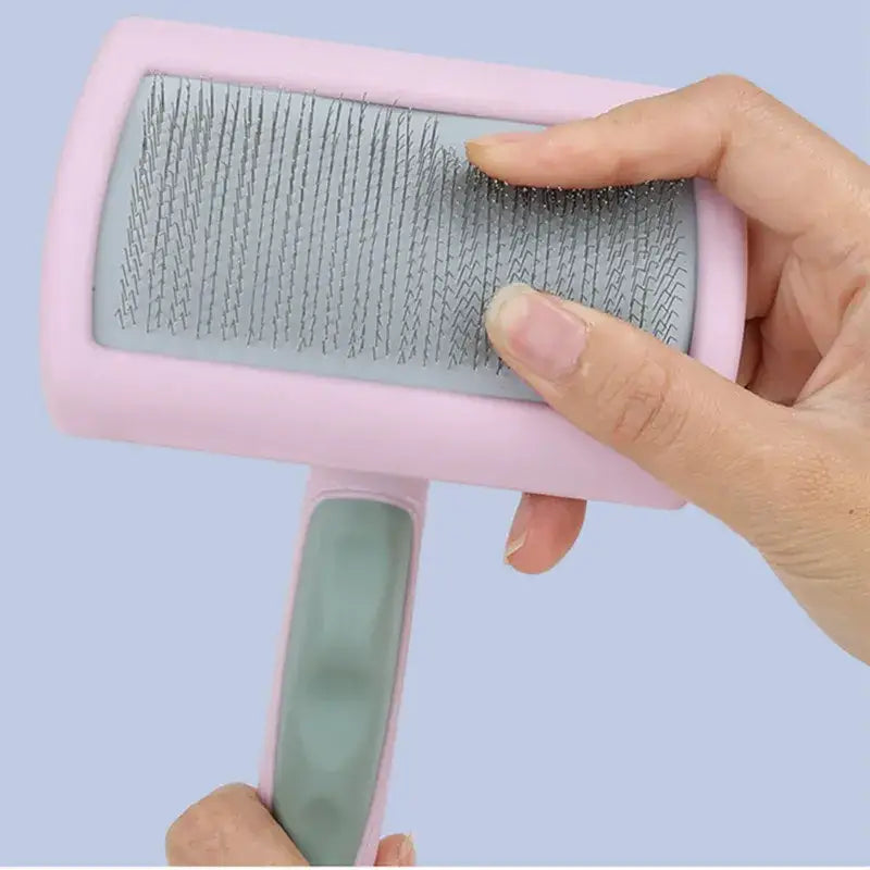 Pet grooming brush with fine metal bristles and a pink plastic handle.